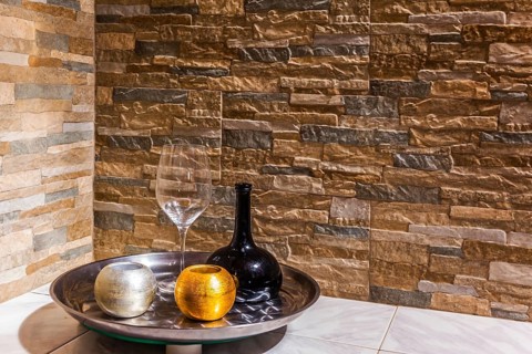 Still-life with a black glass jug, a transparent glass and two candlesticks. Background stone wall.