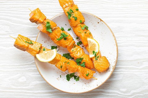 Grilled barbecue salmon skewers seasoned with green parsley and lemon on ceramic plate on white