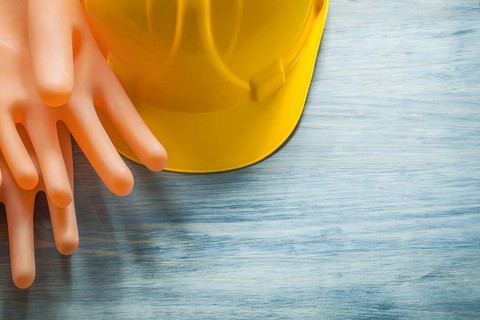 Pair of rubber insulating gloves building helmet on wooden board electricity concept