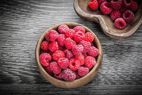 Round and heart-shaped bowls with ripe raspberries on wooden board