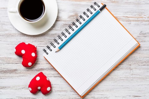 Coffee cup notepad pencil and two red hearts on wooden surface