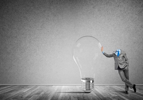 Headless businessman in empty room leaning on glass light bulb