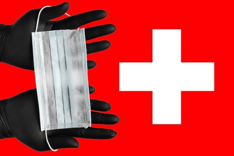 Doctor holds face mask in hands in black medical gloves on background colors flag of Switzerland.