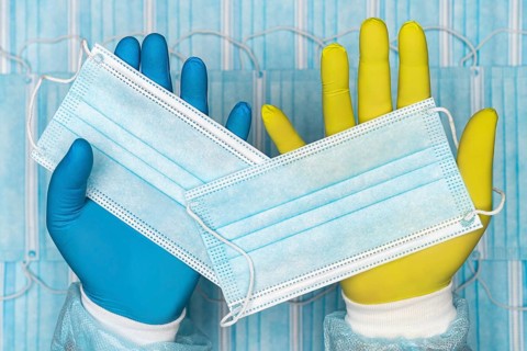 Doctor holds medical face mask in blue glove in one hand and other surgical face mask in yellow