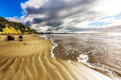 New Zealand. Moeraki's huge round boulders on a sandy beach. The Pacific ocean tide begins. The