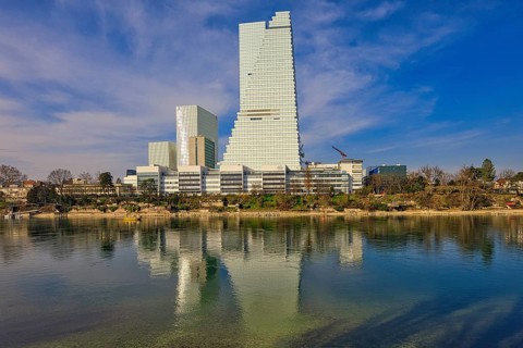 Towering buildings are reflected in the calm water under a blue sky, pharmaceutical company Roche,