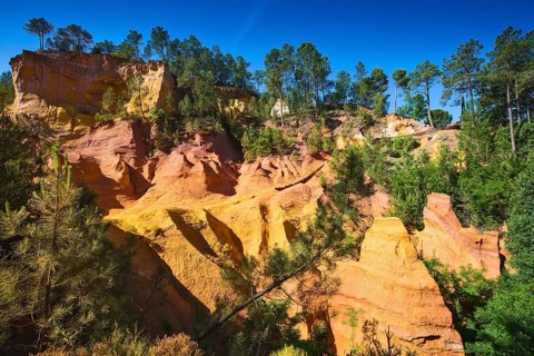 Unique red and orange hills in the province of Languedoc - Roussillon, France. Green trees create a