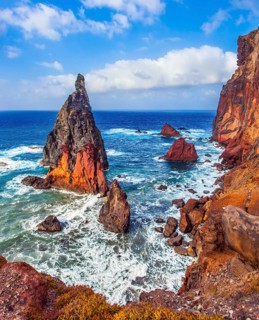 The sharp red rocks, boiling turquoise surf. The blinding midday sun illuminates the rocky shore.
