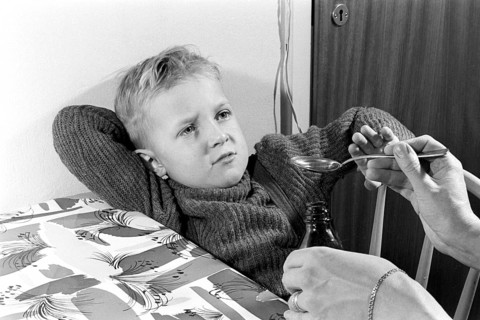 A boy is sick and won't take his medicine. His mother holds out a spoon and waits for him to gape