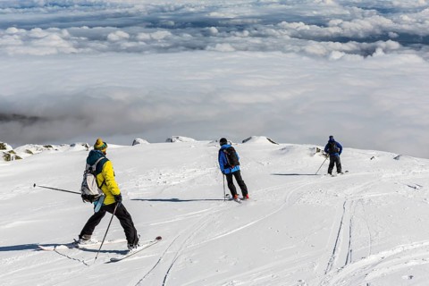 Three free riders are prepairing for skiing down a snowy rocky mountain top