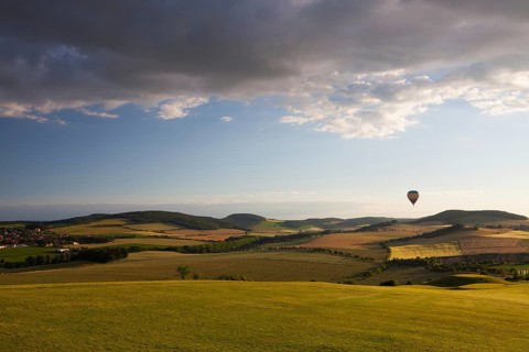Hot air balloon flying over a golf course and amazing valley at sunset
