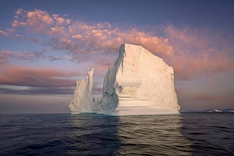 Large glaciers in the bay by the rocky shore in the light of the setting sun
