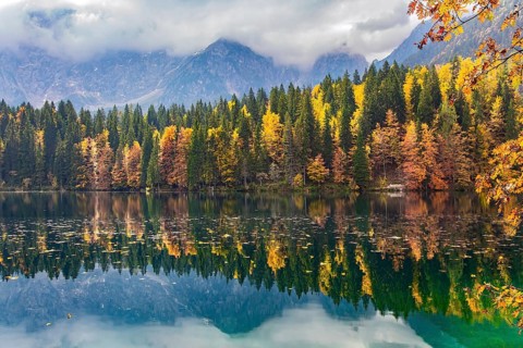 The colors of the autumn forests are reflected in the icy water of the lake. Sunrise. Mountains