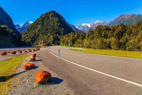 Snowy peaks of rocks are visible in the distance. Wonderful summer day. Great highway among fields,