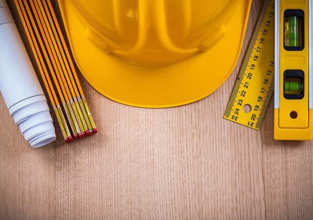 Protective helmet instruments of measurement blueprints and construction level on wooden board