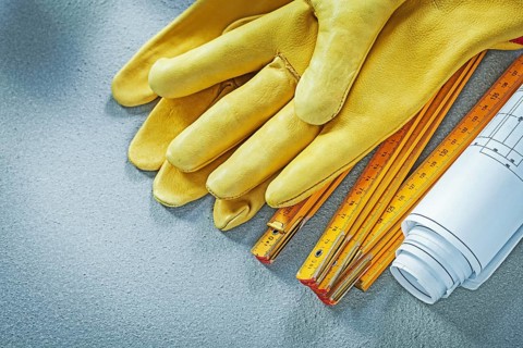 Protective gloves blueprints wooden meter on concrete background building concept