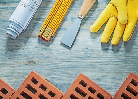 Assortment of red bricks safety gloves palette knife blueprints wooden meter building concept