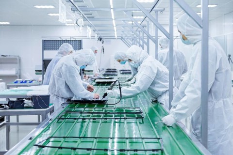 Factory workers in white lab suits and face masks, producing tv sets on a green assembly line with