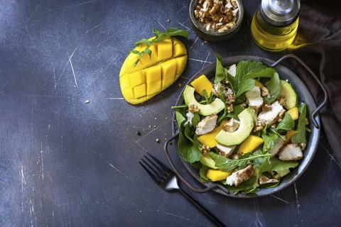 Healthy diet salad with arugula, mango, avocado, chicken grill, walnuts and vinaigrette dressing on