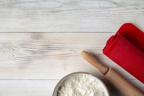 Cup with flour, rolling pin, cooking mat on wooden table, copy space
