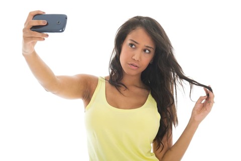 Young attractive black woman is taking a selfie with her cellphone isolated over white background