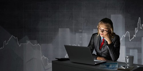 Attractive young businesswoman in glasses sitting at office desk and working at laptop. Female