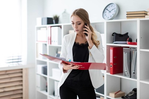 Beautiful young girl with blond hair in a white jacket and black blouse is working in the office.