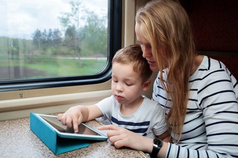 Mother and her little son using touchpad sitting by the window in the train