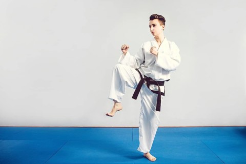Girl in karate suit kimono in studio at grey background. Female child shows judo or karate stans in