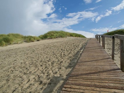 A long wooden walkway leads up sandy dunes, with a sky of clouds and blue, Juist, East Frisia,