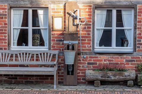 Rustic brick wall with two windows, old water pump and bench against a rural backdrop, gemen,
