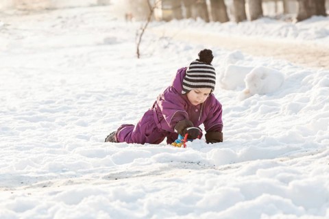 Boy playing with snowplow toy. Cold winter day