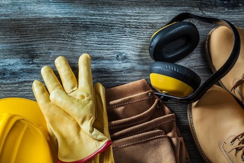 Leather protective gloves boots tool belt hard hat earmuffs on wooden board