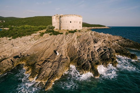 Bride and groom stand on the rocks near the fortress by the sea. Aerial view.