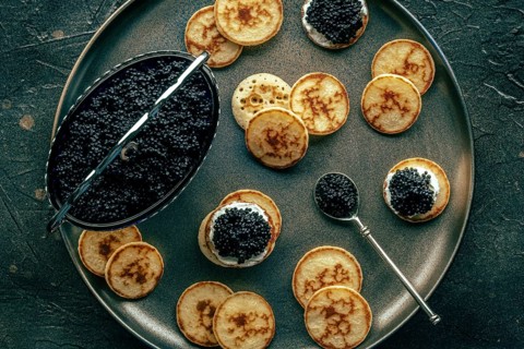 Blinis with caviar, overhead flat lay shot on a festive dish, mini pancakes, an elegant appetizer,