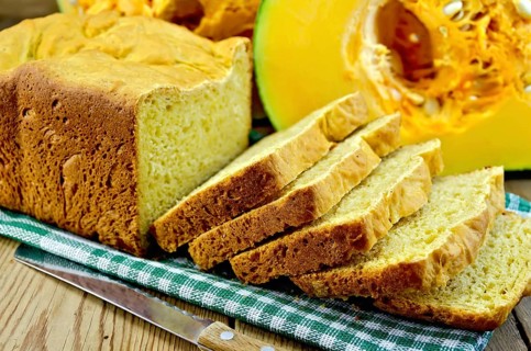 Homemade pumpkin bread on a green napkin, cut pumpkin, knife on background wooden board