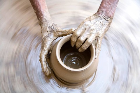 Pottery, artist muddy hands making clay pot giving shape on spinning wheel, semi urban village