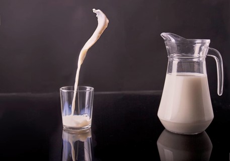 Glass jug and cup filled with white milk. Pouring organic drink in motion