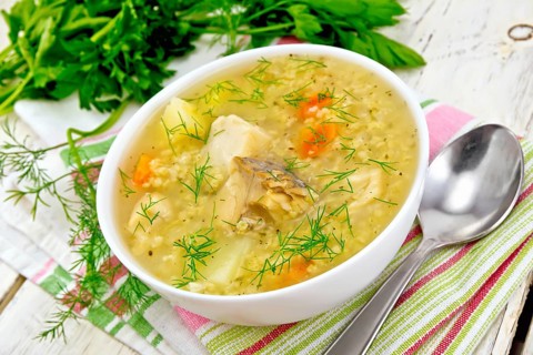 Soup fish kulesh with millet, potatoes and carrots in a white bowl on a napkin, parsley, dill on a