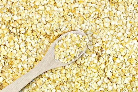 Texture of yellow pea flakes with a wooden spoon