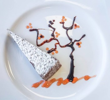 A typical italian slice of cake caprese made of chocolate and almonds with decorative tree made of