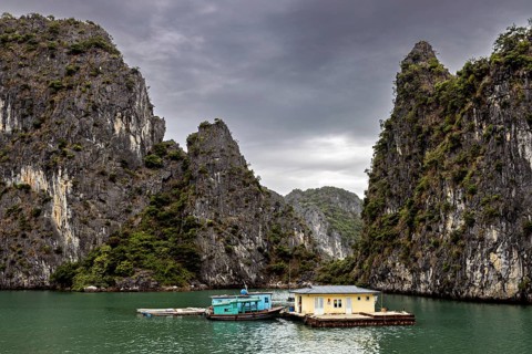 Single houseboat between towering limestone cliffs under a grey sky, The floating villages in