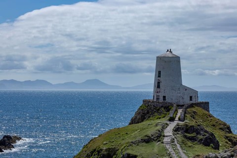 Twr Mawr Lighthouse, white lighthouse on a hill by the sea with blue sky and clouds, Ynys