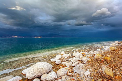 Rocky beach covered with evaporated salt. The Dead Sea is a closed salt lake. Gloomy sky with dark