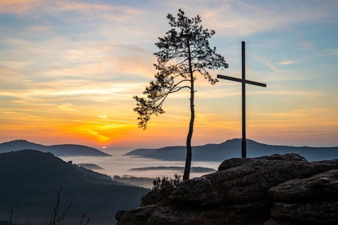 Landscape shot of nature in the morning. Mist in the valley and a summit cross on a sandstone cliff