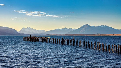 A peaceful coastal landscape with mountains in the background and an old wooden jetty in the sea,