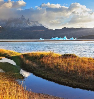 Gray lake and snow-capped mountains. Blue iceberg floating in the distance. Warm summer sunset