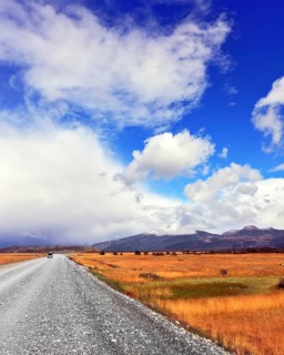 The dirt road in the endless pampas. Strong wind drives the clouds. See the mountains on the