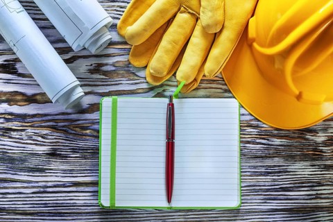 Blueprints notepad pen building helmet safety gloves on vintage wooden board