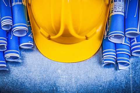 Blue rolled engineering drawings yellow building helmet on metallic background construction concept